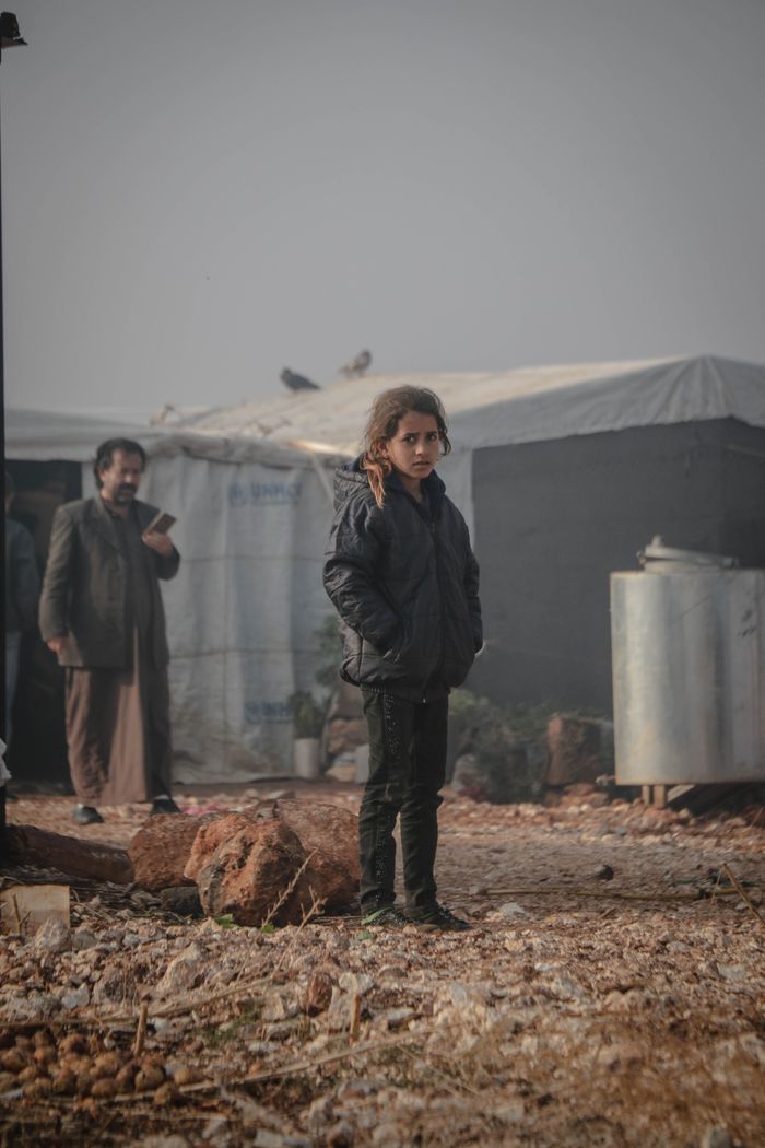 why-choose-us-02 A young girl stands outside a makeshift shelter in Idlib, Syria.