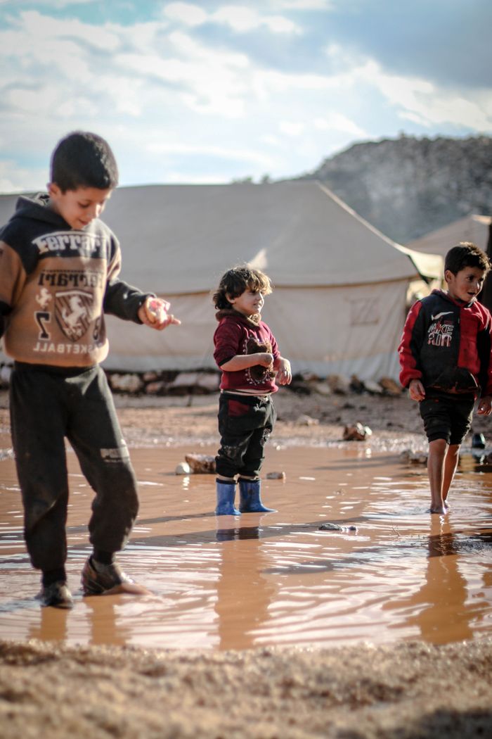 why-choose-us-01 Children enjoying playtime in a muddy puddle at a refugee camp in Idlib, Syria.