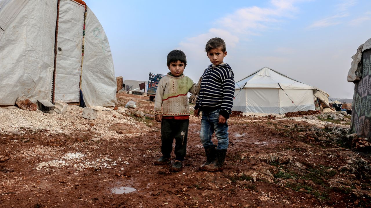 our-story-02 Two children standing in a muddy Syrian refugee camp in Idlib.